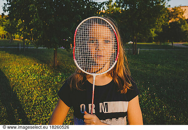 Girl is looking through a badminton racket in the park on a summer day