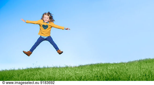 Girl jumping for joy on grassy hill