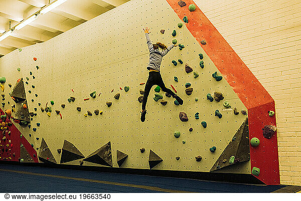 girl jumping off a bouldering wall at a climbing centre indoors