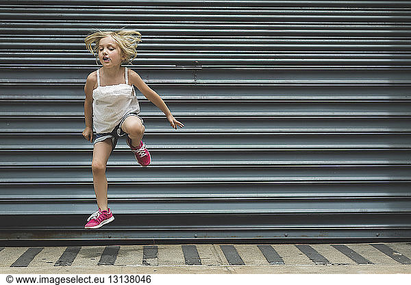 Girl jumping on sidewalk against shutter