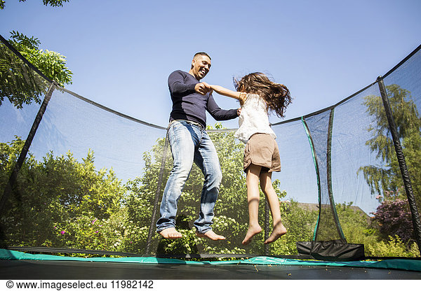 Girl (6-7) jumping on trampoline with father