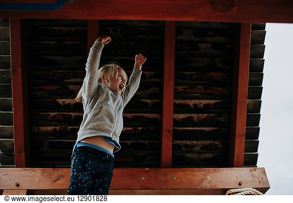 Girl jumping with arms raised on playground platform
