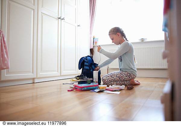 Girl kneeling on floor packing school bag