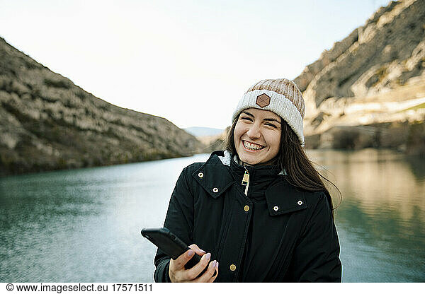 girl laughing while holding her cell phone next to a lake