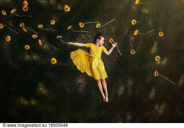 Girl laying in grass surrounded by sunflowers