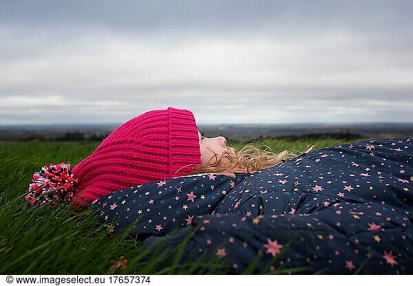 girl laying in the grass in a field watching the clouds in the sky