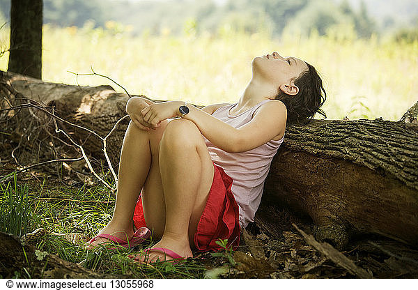 Girl leaning head on fallen tree trunk while sitting in field