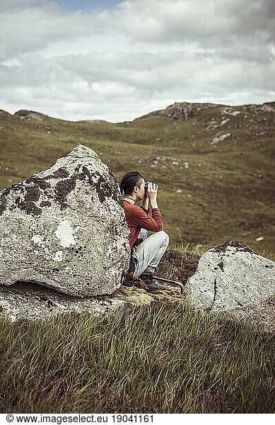 girl leans on rock with binoculars