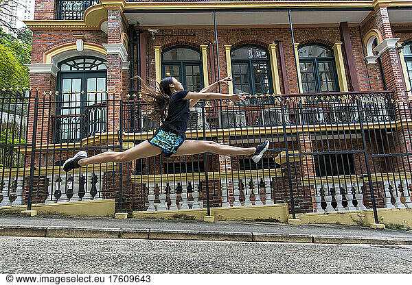 Girl leaping in mid-air in front of a building in a public park; Hong Kong  China