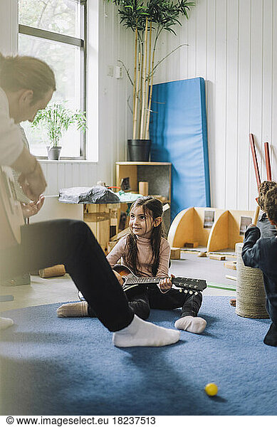 Girl learning guitar from male child care worker at kindergarten