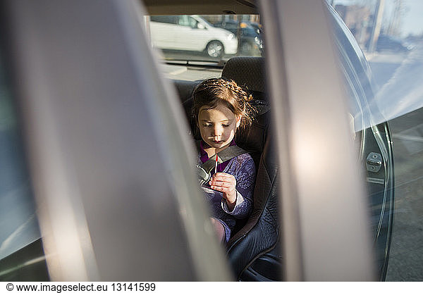 Girl looking at lollipop while sitting in car seen through vehicle door