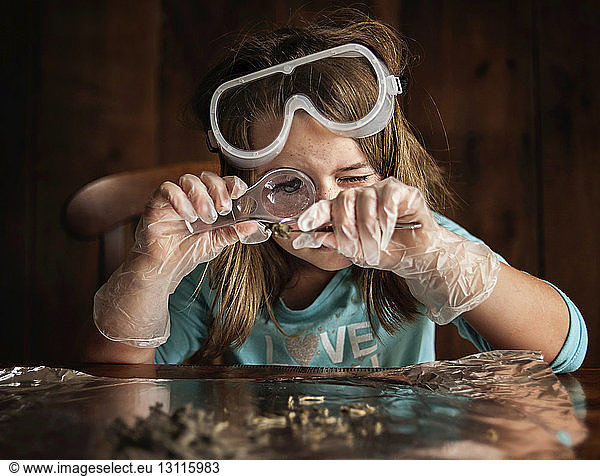 Girl looking at object through magnifying glass while sitting at table