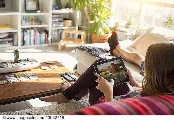 Girl looking at pictures in tablet computer while sitting on sofa