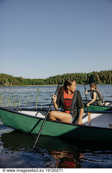 Girl looking away while sitting in kayak on lake at summer camp
