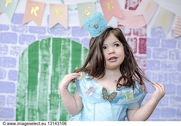 Girl looking away while standing against castle painting during princess party