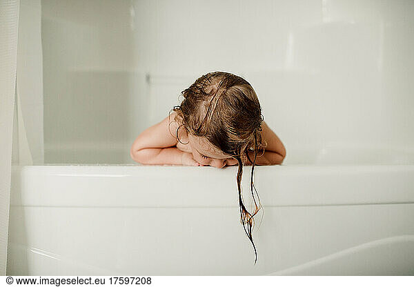 Girl looking down leaning on white bathtub