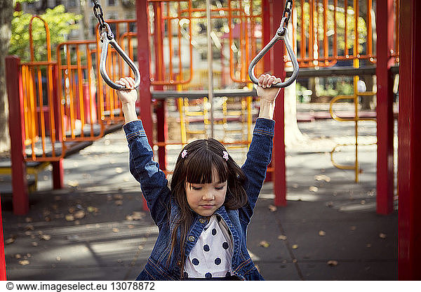 Girl looking down while hanging on monkey bars in park