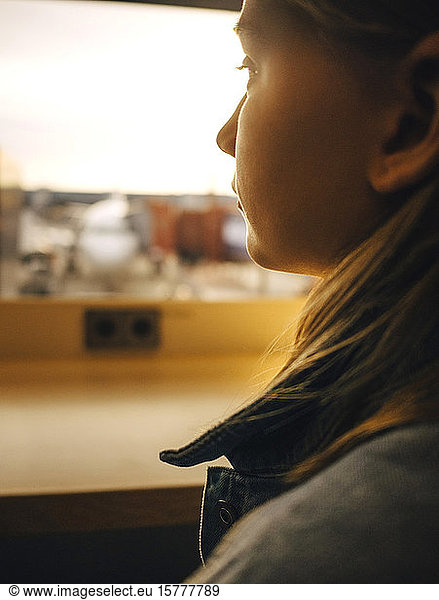 Girl looking through window while sitting at airport