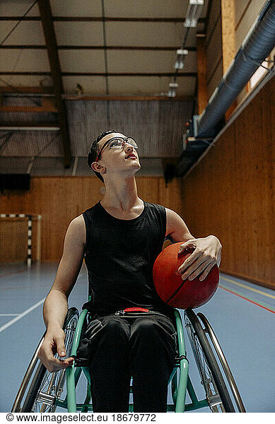 Girl looking up while sitting on wheelchair with basketball at sports court