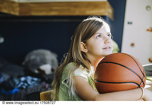 Girl looking up while sitting with basketball at home