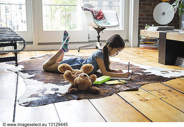 Girl lying on carpet and writing on book at home