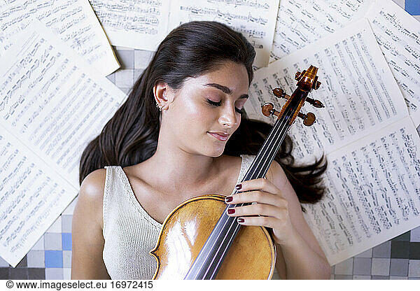 Girl lying on the floor with a viola and surrounded by musical scores.
