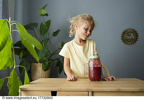 Girl making puckering face looking at smoothie in living room