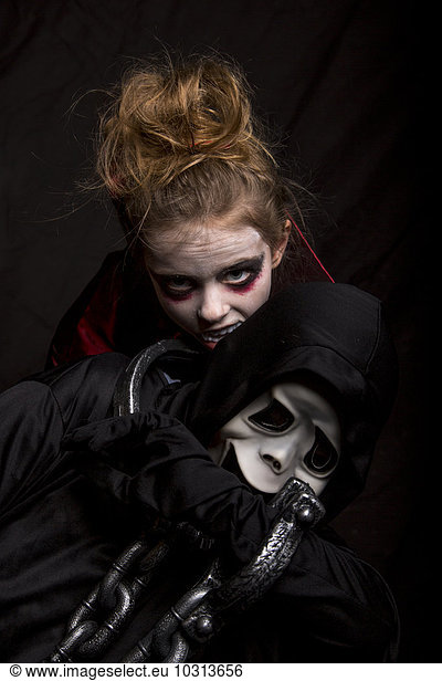 Girl masquarade as vampire biting boy wearing Scream mask