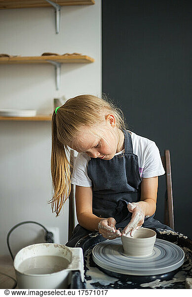 Girl modelling clay on a potter's wheel in the pottery workshop.
