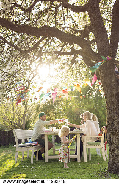 Girl (18-23 months) and family sitting at picnic table