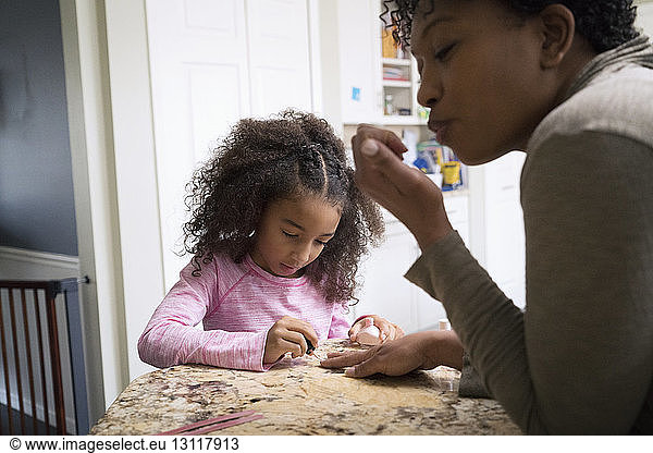 Girl painting mother's fingernails at home