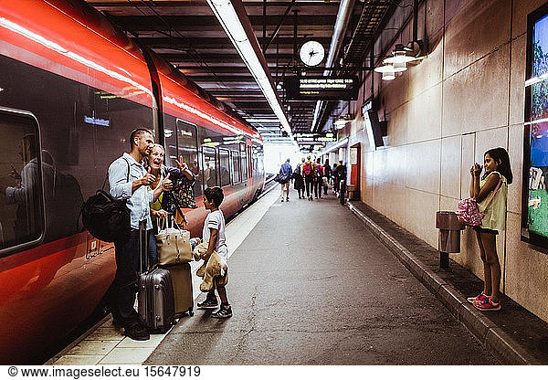 Girl photographing family standing with luggage against train at railroad station