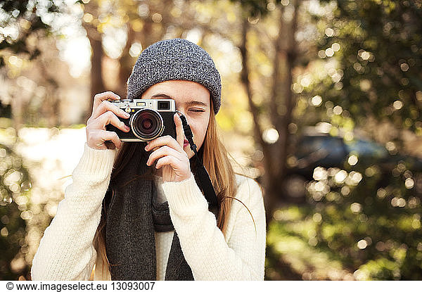 Girl photographing with camera against trees