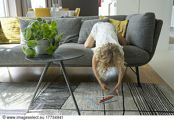Girl picking up colored pencils from carpet at home