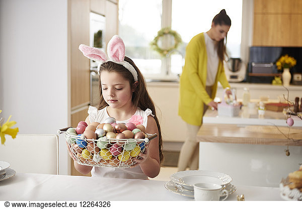 Girl placing basket full of Easter eggs on dining table