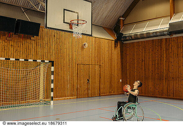Girl playing basketball while sitting on wheelchair at sports court