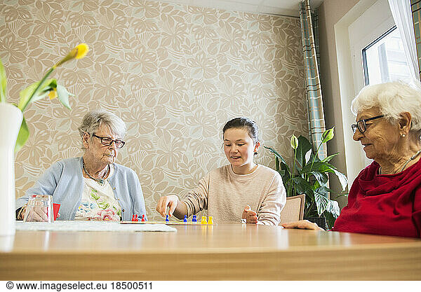 Girl playing board game with senior women in rest home