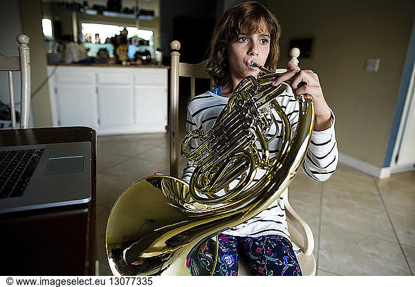 Girl playing French horn while sitting on chair at home