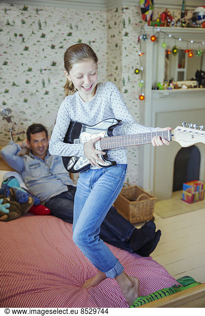 Girl playing guitar for father in bedroom