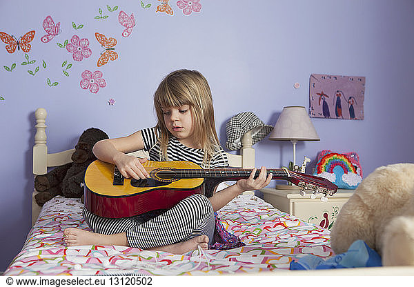 Girl playing guitar on bed at home