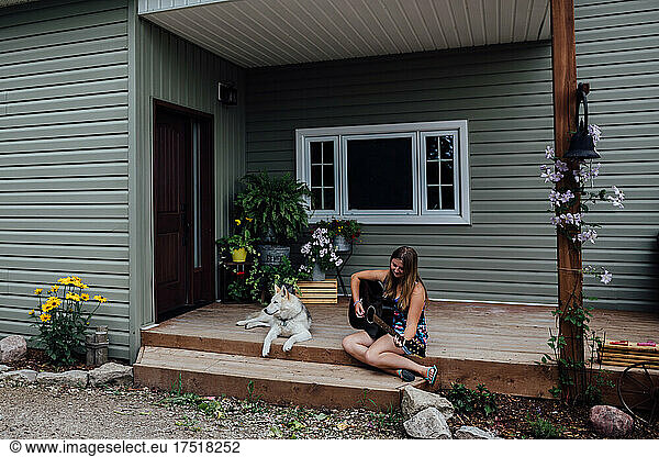 Girl playing guitar on the porch with pet dog