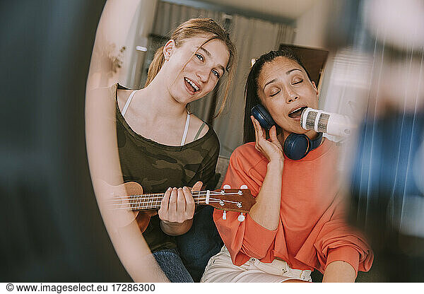 Girl playing ukulele while woman singing on microphone at home