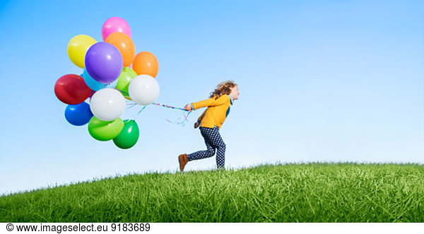 Girl playing with balloons on grassy hill