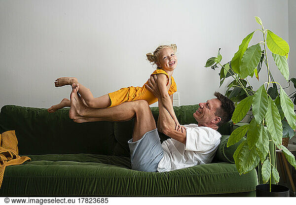 Girl playing with father lying on sofa at home