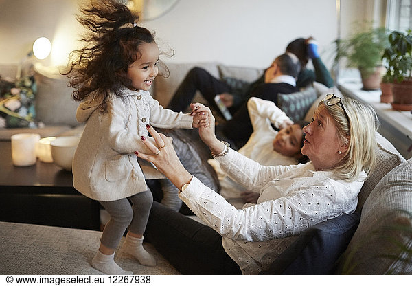 Girl playing with grandmother on sofa by family at home