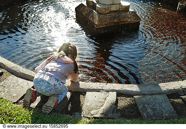 Girl playing with water in public park pond