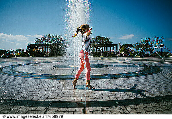 Girl plays in water fountain on hot summer day