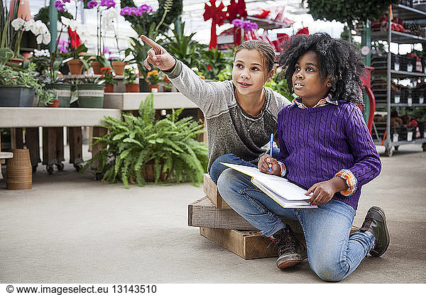 Girl pointing while sitting with friend in plant nursery