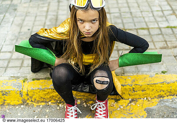 Girl posing in super heroine costume sitting on curb