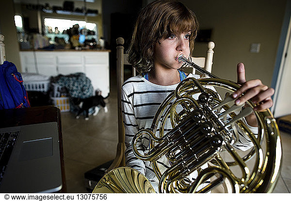 Girl practicing French horn while sitting on chair at home